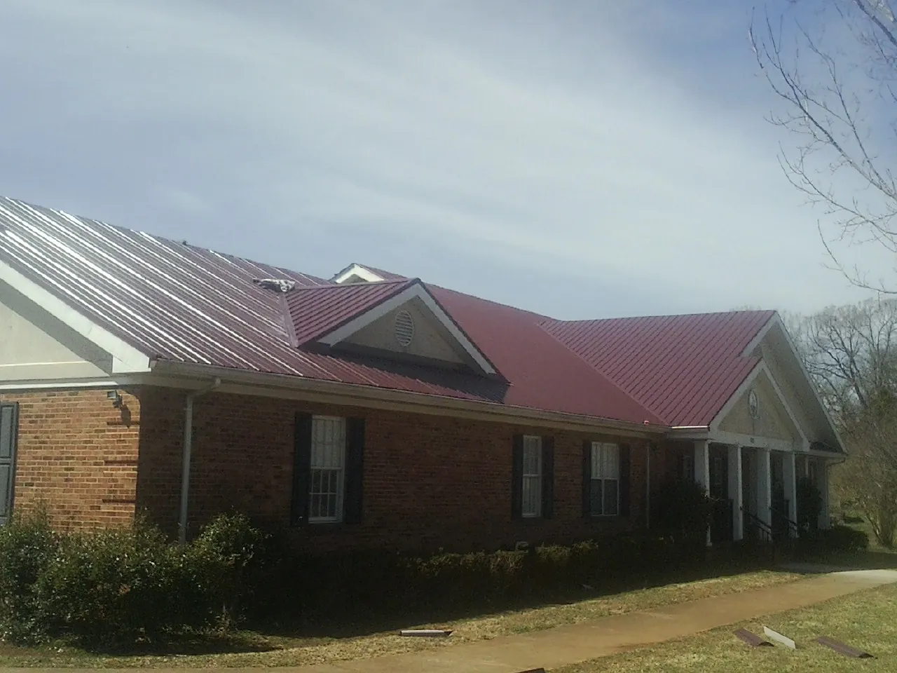 Red metal roof with gabled entries on a long brick building, from a Hail Damage Roof Repair job in Coulee City