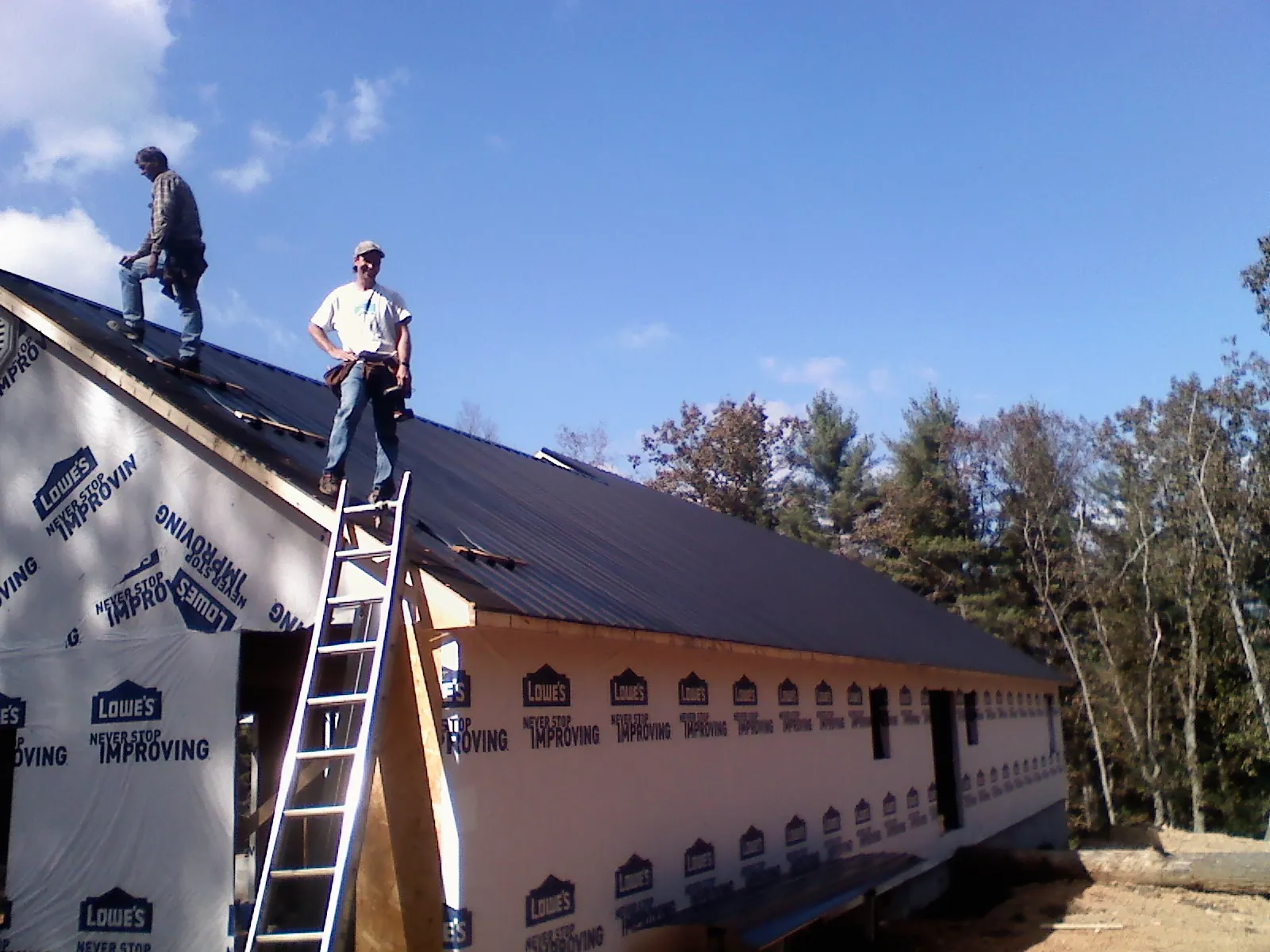 Two roofers standing on a long dark metal roof over a wrapped building in Coulee City