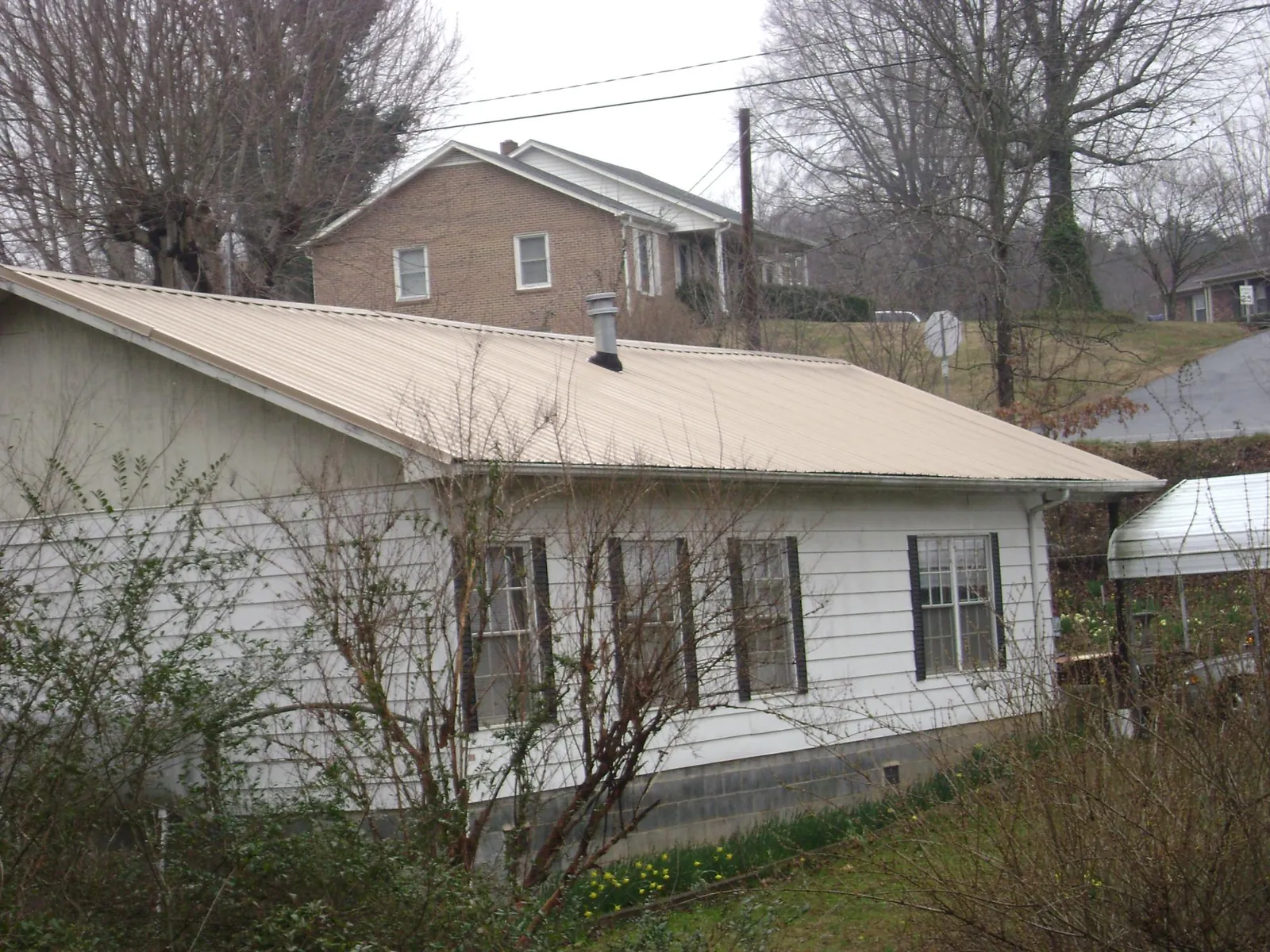 Tan metal roof on a white sided house set into a hillside — Commercial Roofing by Roofing Brothers in Coulee City